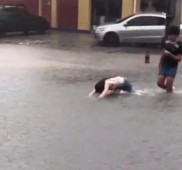 Crianças mergulham em rua alagada durante forte chuva em João Pessoa